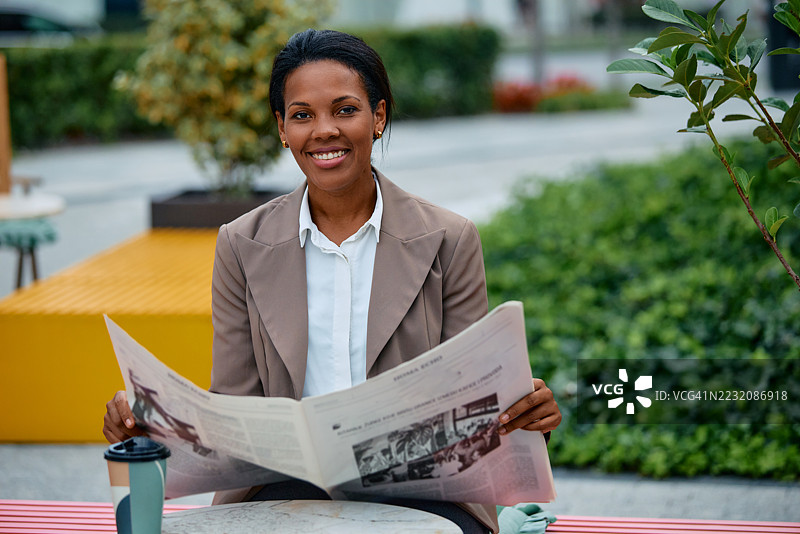 微笑的女商人在长椅上阅读报纸图片素材