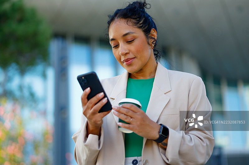 职业女性在现代企业外部查看智能手机，喝咖啡。图片素材