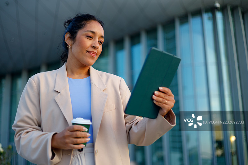 专业女性在现代摩天大楼附近使用平板电脑，喝着咖啡，穿着职业装图片素材