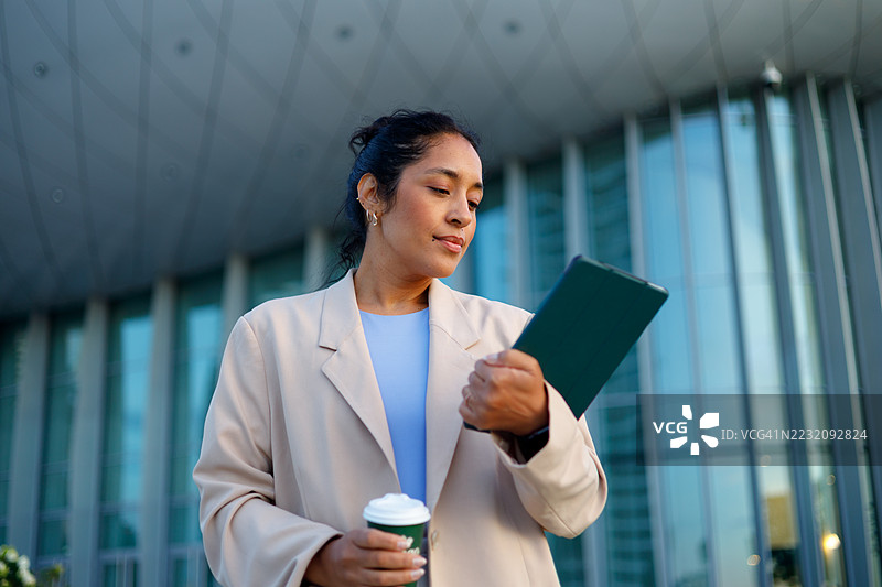 女商人在现代办公大楼外一边喝咖啡一边阅读数字平板上的信息图片素材