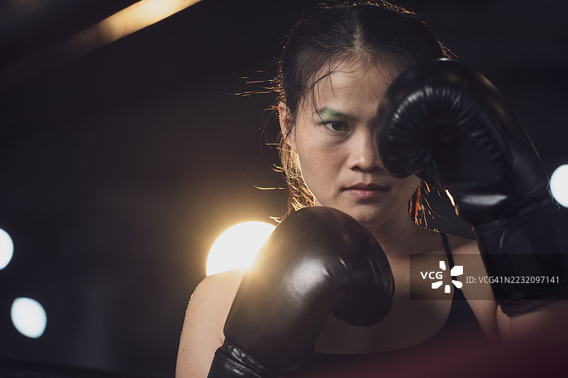 年轻的亚洲女性踢拳手正在练习攻击动作。她戴着手套，像在打斗一样出拳。图片素材