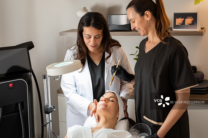 年轻女性在皮肤科医生和美容师的指导下进行面部美容治疗图片素材