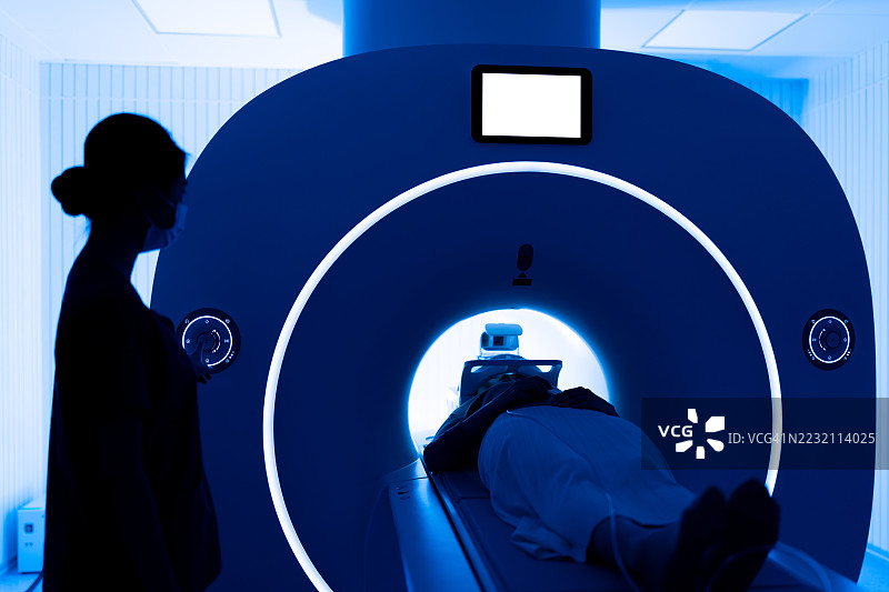 年轻的亚洲女性护士在MRI扫描室操作MRI扫描仪。女性医疗工作者在医学扫描室内。蓝色调。图片素材