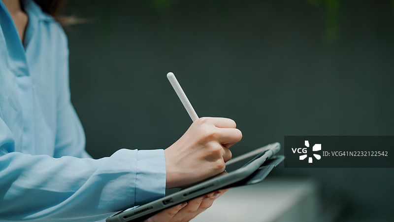 女性在办公楼的户外公共区域使用平板电脑工作。图片素材