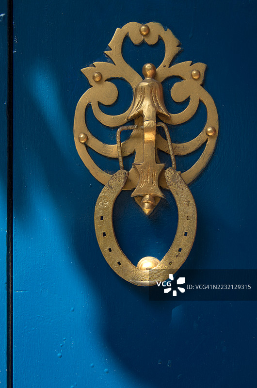 蓝色的木门上饰有华丽的金色马蹄铁门环图片素材