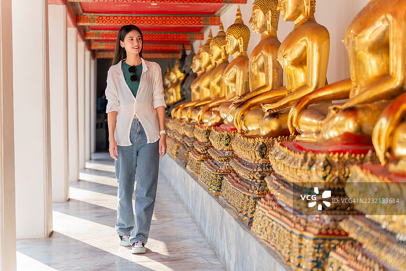 一名游客在泰国宁静的寺庙走廊里，走过金色的佛像图片素材