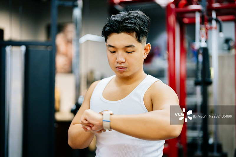 亚洲年轻男子在健身房训练后查看健身追踪器上的数据。健康与健身概念。图片素材