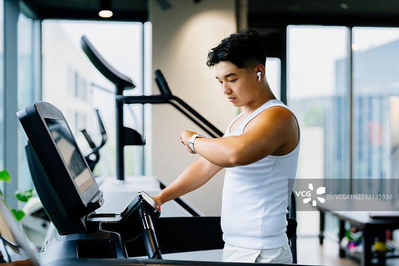 亚洲年轻男子在健身房锻炼时查看健身追踪器上的数据。健康与健身概念。图片素材