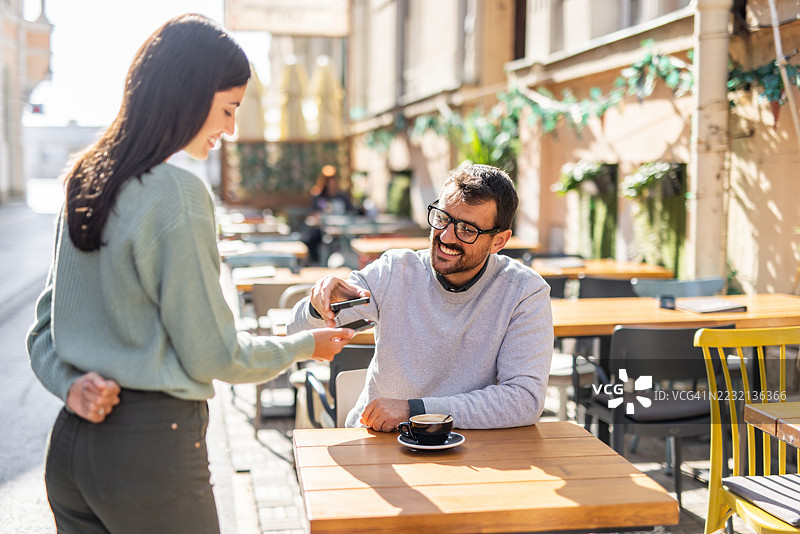 顾客在户外咖啡馆使用手机进行无接触支付图片素材