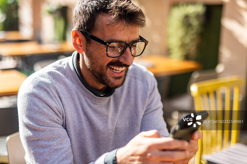 快乐的企业家在户外咖啡馆使用智能手机图片素材