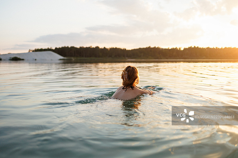 女人在日落时分的清澈湖水中游泳图片素材