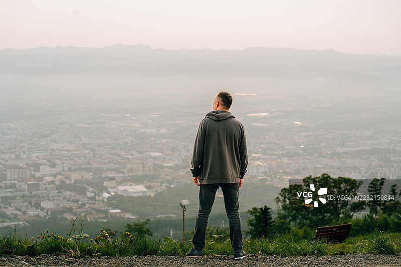 男人在萨哈林地区的山顶上沉思城市风景，夕阳西下。图片素材