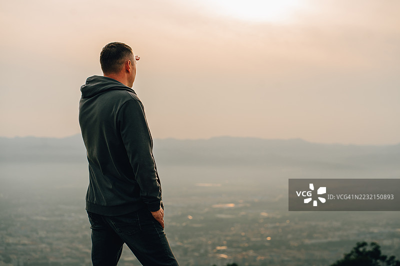 男人在日落时分从山顶俯瞰城市风景图片素材