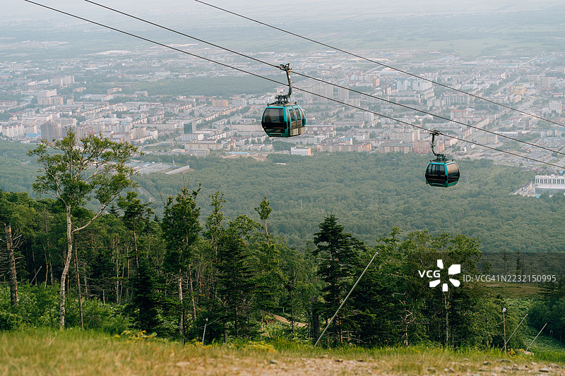 缆车穿过绿色森林，背景是城市风景图片素材