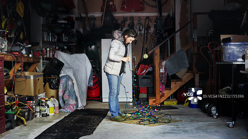 女人在杂乱的车库里理顺纠结的圣诞灯，为节日做准备图片素材