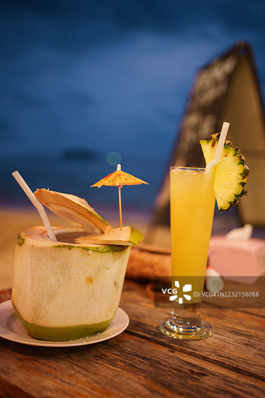 海滩度假时黄昏的清爽椰子饮料和菠萝鸡尾酒图片素材