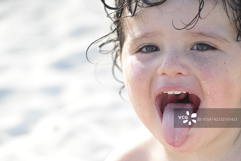 在海滩上，顽皮的孩子用满是沙子的脸 sticking out tongue。图片素材