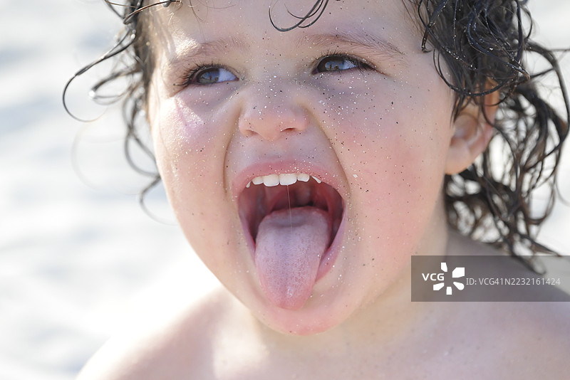 在海滩上，顽皮的孩子满脸沙子，吐着舌头。图片素材