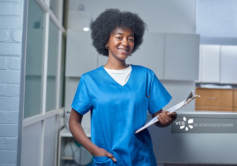 微笑的护士穿着工作服，在诊所接待区手持夹板图片素材
