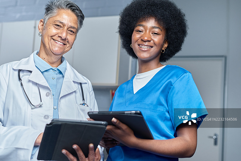 两位微笑的医疗专业人员在诊所接待区使用平板电脑图片素材