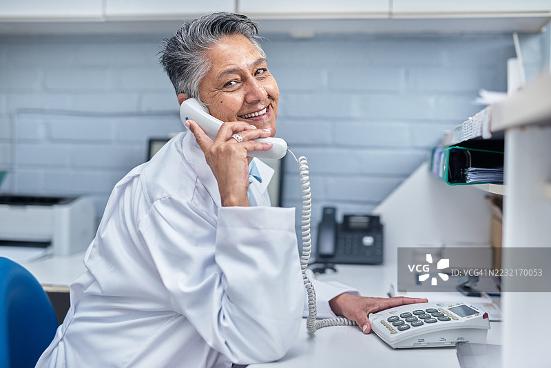 友好的医疗专业人员在医疗环境的接待台接听电话图片素材