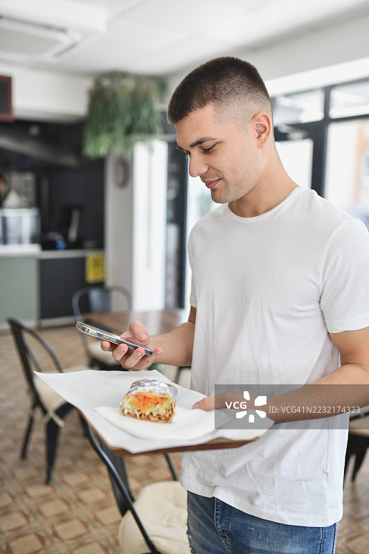 帅气的男人手持托盘，托盘上放着土耳其烤肉，同时随意地滑动智能手机。图片素材