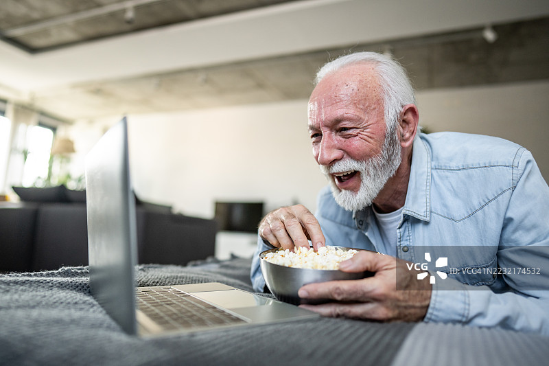 快乐的老年男子在家里看电影，边吃爆米花边享受时光图片素材