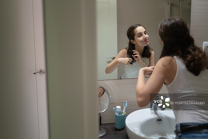 年轻女性在浴室镜子前整理头发图片素材
