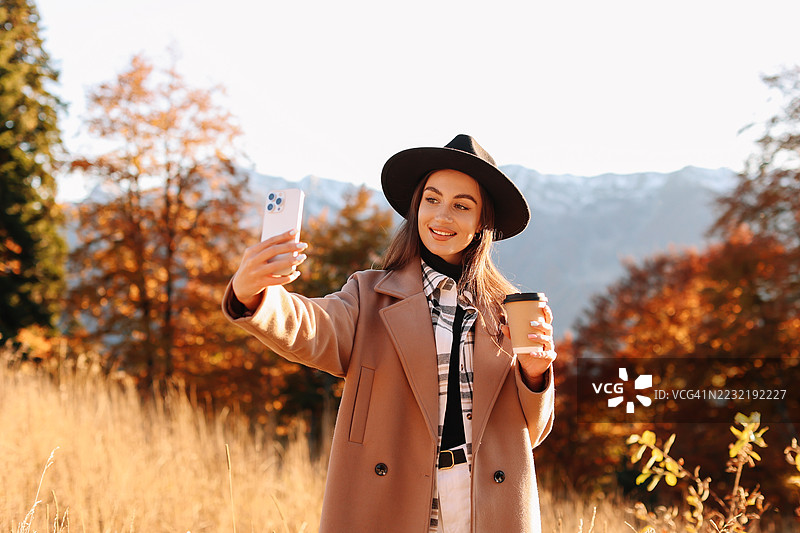 身着秋季外套和帽子的美丽年轻女子在自然小径上穿过黄色的森林图片素材
