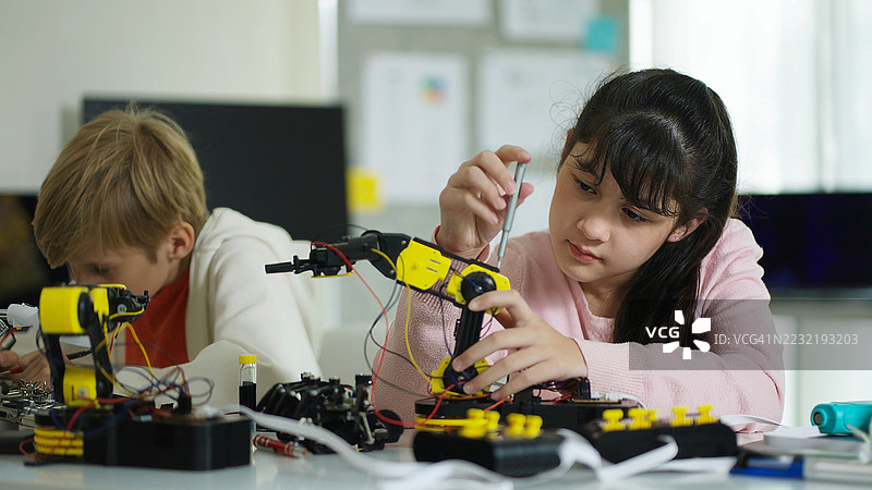 在充满活力的学校环境中，多元化的学生们齐心协力地研究机械臂和电子元件，展现出团队合作与创造力。图片素材