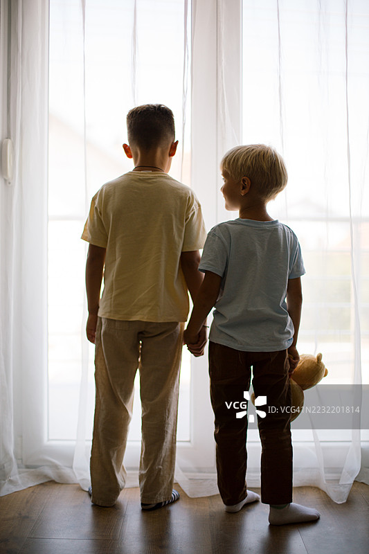 两个兄弟手牵手，望着窗外。图片素材