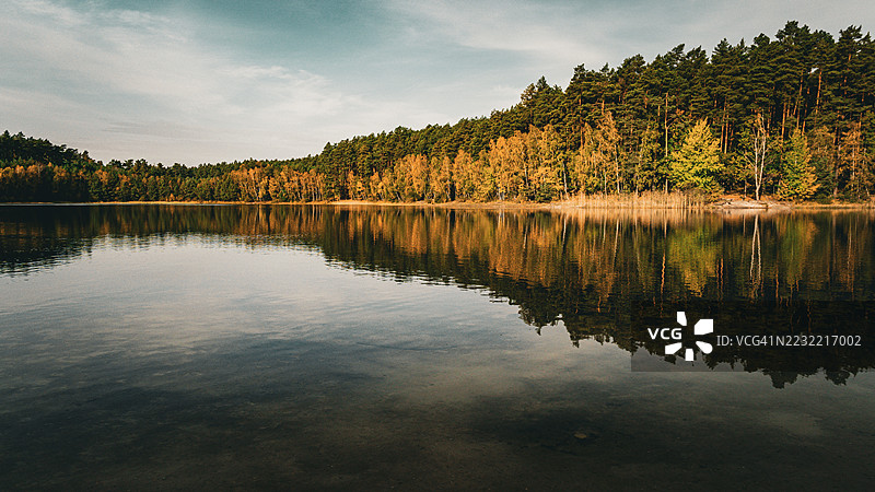 宁静的湖泊被秋季森林环绕，水中倒映着景色，波兰马诺沃图片素材