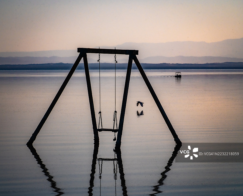 秋千架在宁静的日落和宁静水面前的剪影，位于美国加利福尼亚州的孟买海滩图片素材