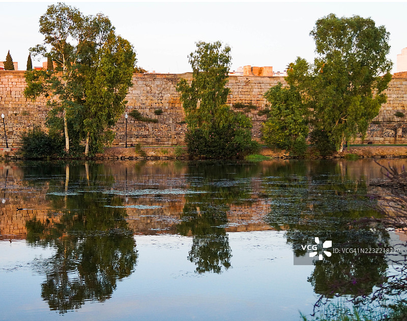 宁静的湖泊映照着古老的石墙和树木，西班牙图片素材