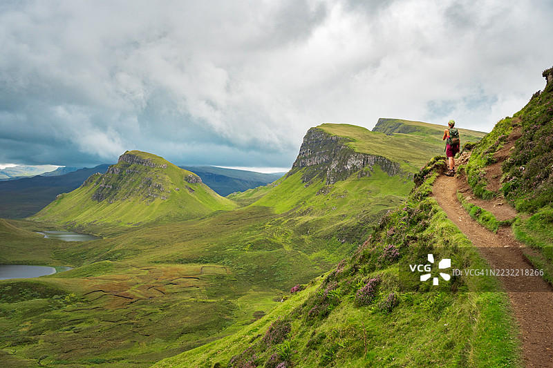 在多云的天空下，英国的一条风景优美的山间小径上，一位女性正在徒步旅行。图片素材
