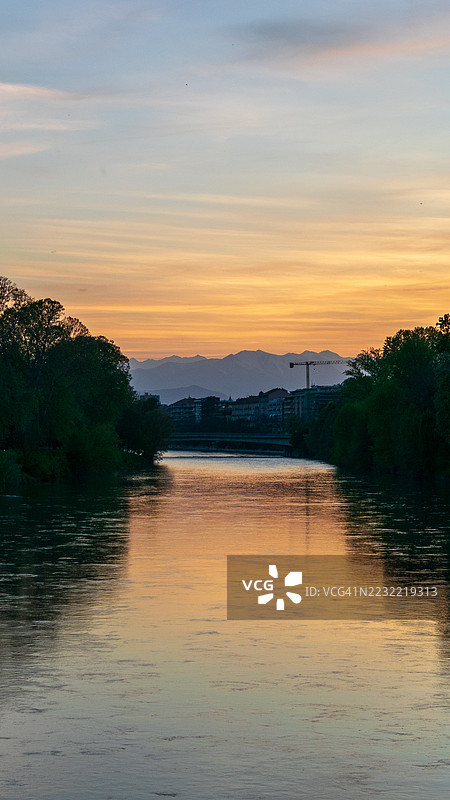 宁静的河流映照着日落的色彩，远处是意大利都灵的山脉图片素材