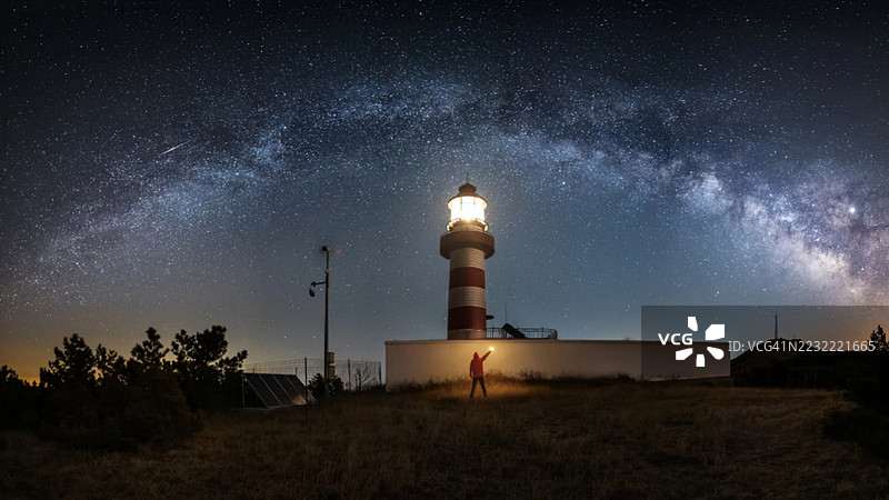 在日本的灯塔附近，仰望星空的观星者，夜空中银河璀璨。图片素材