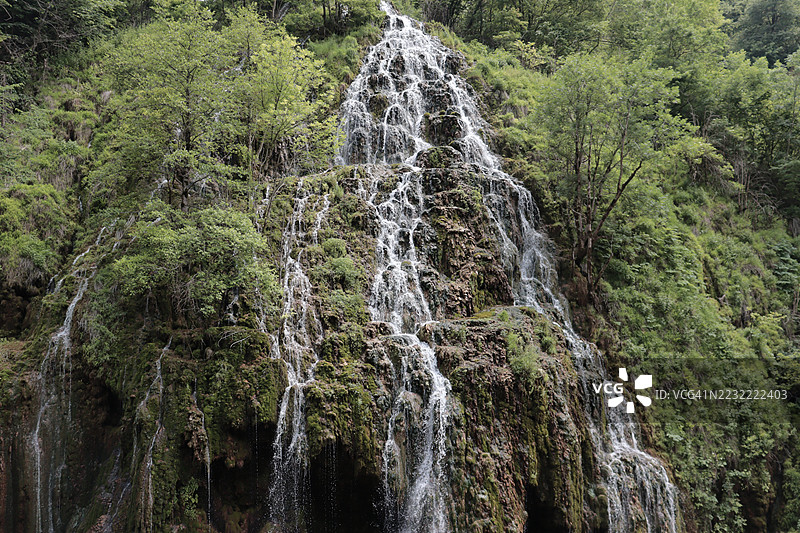壮观的瀑布倾泻而下，穿过郁郁葱葱的森林图片素材