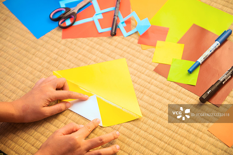 在桌子上用手折叠五彩纸，周围有手工艺材料图片素材