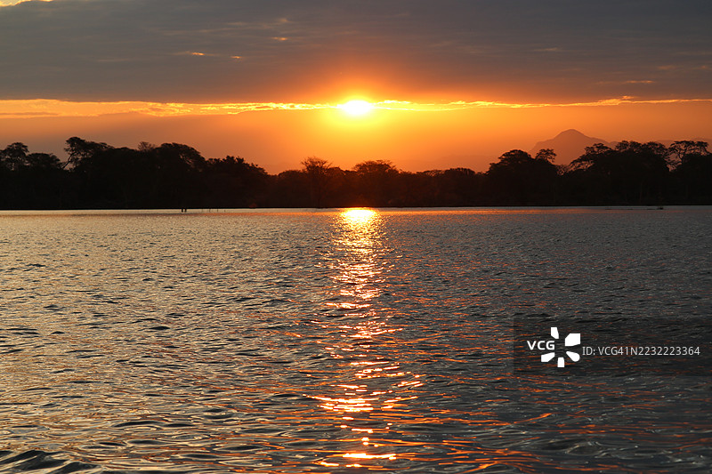 宁静湖面上的日落与剪影树木图片素材