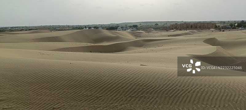 广阔的沙漠景观，沙丘与远处的建筑，印度杰伊萨尔梅尔图片素材
