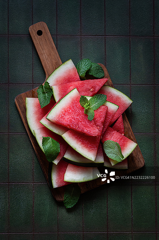 木板上放着西瓜和薄荷，背景为绿色。图片素材