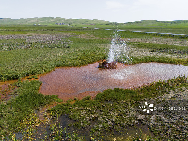 在亚美尼亚希拉克省卡尔马拉万附近的广阔绿色景观中，喷涌而出的喷泉与红色水面，鸟瞰图。图片素材