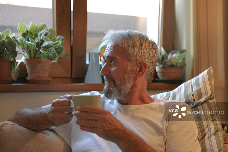 成熟男性在窗边放松，手中捧着热饮图片素材