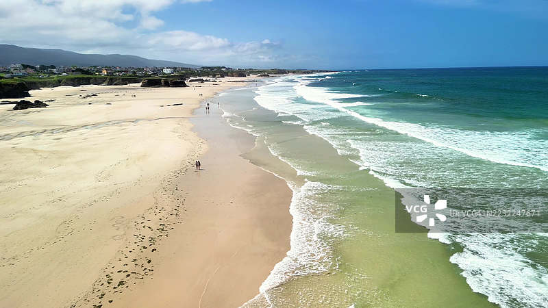 沙滩的鸟瞰图，海浪拍打着岸边，远处是连绵的山丘图片素材