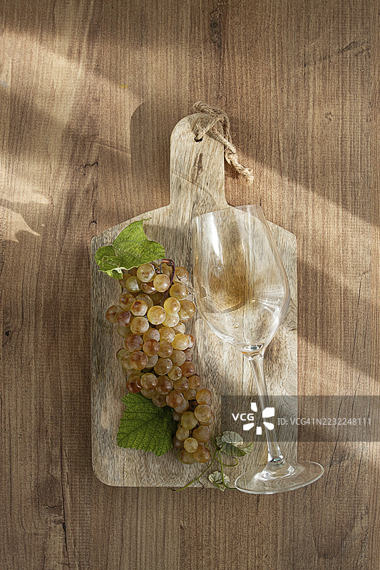 一串白葡萄，放在木板上，旁边有一杯白葡萄酒，俯视图，自然光照，食品概念，无人。图片素材