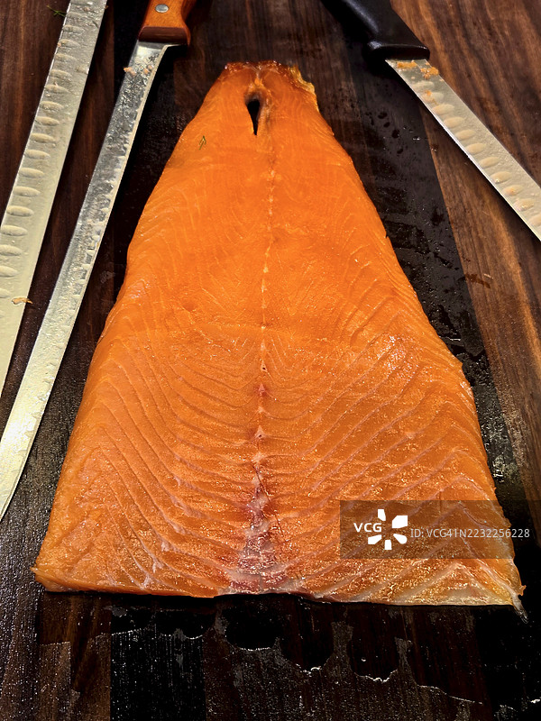 整条熏鲑鱼鱼片放在木板上，旁边有刀具图片素材