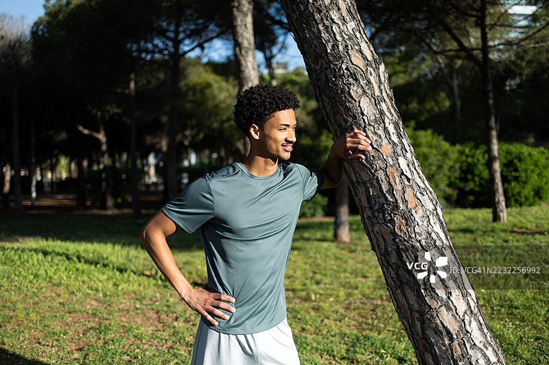 年轻运动员在公园里靠着树休息，训练后放松。图片素材
