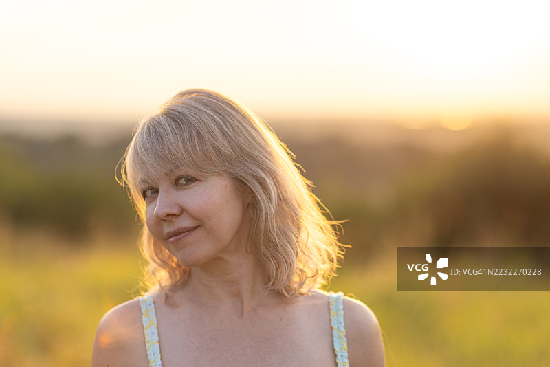 日落时分，户外微笑的女性肖像，阳光洒在她的头发上图片素材