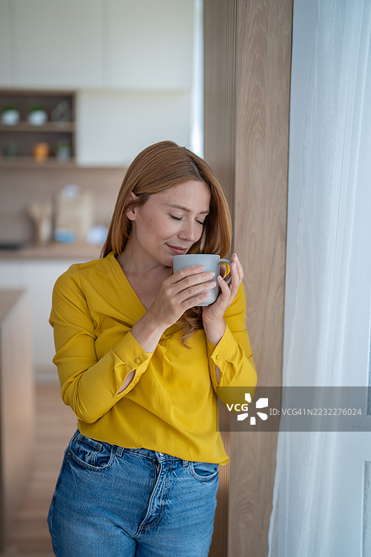 宁静的女人在厨房窗边享受一杯温暖的咖啡图片素材